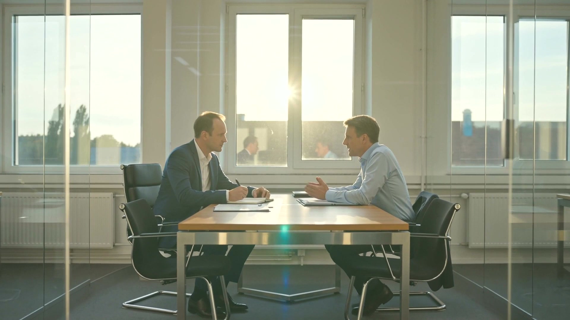 Zwei Personen im Gespräch an einem Besprechungstisch vor einer Fensterfront
